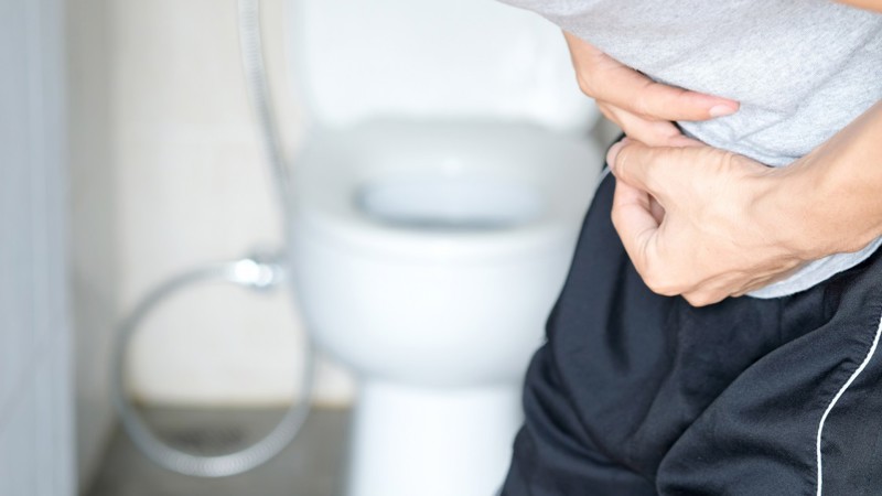 Man with stomach cramp standing next to toilet