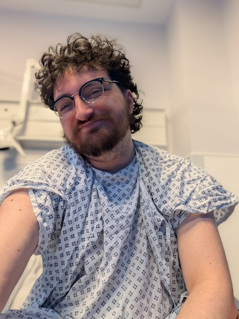 Tony wearing a hospital gown and smiling at the camera.
